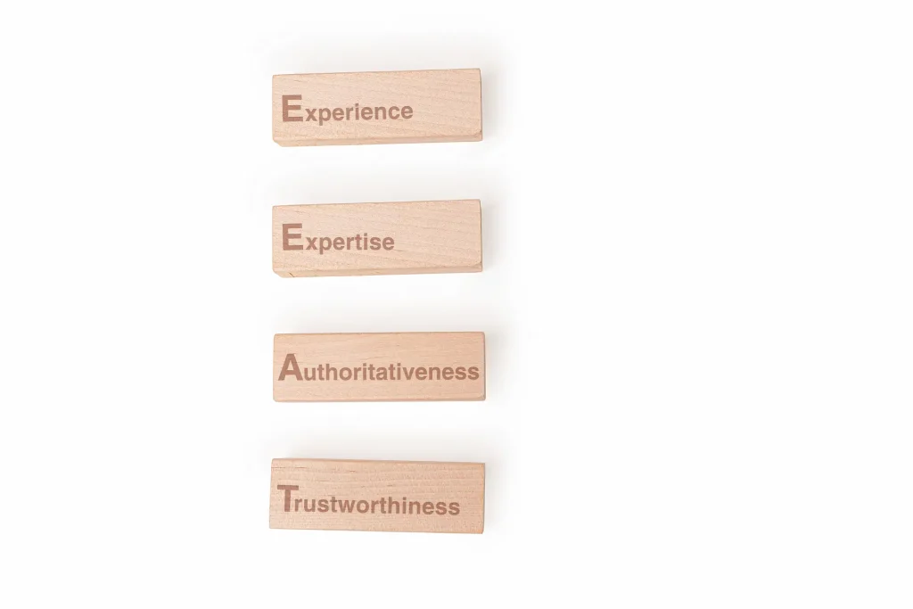 Stacked wooden blocks with the words "Experience," "Expertise," "Authoritativeness" and "Trustworthiness" highlighted against a simple backdrop. Symbolising E-E-A-T values in SEO